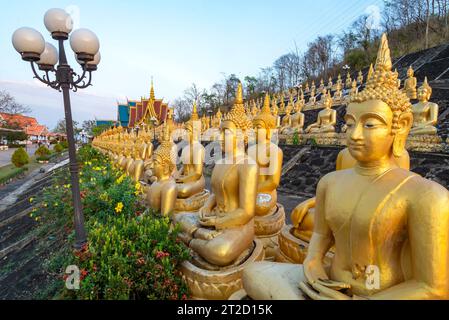 Rangées de belles, miniatures, sculptures d'or vibrantes de Bouddha, illuminées par le soleil couchant, alignées au sommet d'un mur en pente, à côté du temple, Banque D'Images