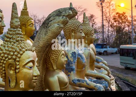 Belles, miniatures, sculptures d'or vibrantes du Saint Bouddha, illuminées par le soleil couchant, alignées au sommet d'un mur en pente, à côté du temple Banque D'Images