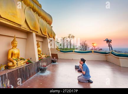 Pakse, sud du Laos-février 17 2023 : au coucher du soleil sur le temple historique de la colline surplombant le fleuve Mékong, une jeune famille bouddhiste laotienne prie. Banque D'Images