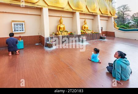 Pakse, sud du Laos-février 17 2023 : au coucher du soleil sur le temple historique de la colline surplombant le fleuve Mékong, une jeune famille bouddhiste laotienne prie. Banque D'Images