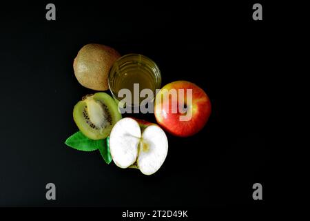 Un grand verre d'un mélange de jus de fruits sur fond noir, une pomme rouge mûre et un kiwi. Gros plan. Banque D'Images