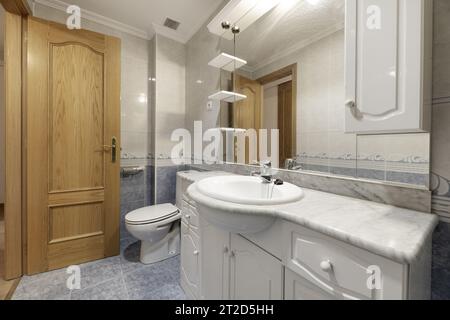 Salle de bains d'une maison avec carreaux bicolores blancs et bleus divisés par une bordure marine, miroir sans cadre sur le mur et lavabo en porcelaine blanche et cou en marbre Banque D'Images