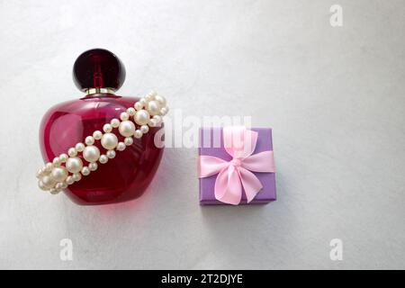 Rose Belle bouteille transparente en verre de parfum féminin décorée de perles précieuses blanches et petit coffret cadeau bleu et place pour un texte simple sur Banque D'Images