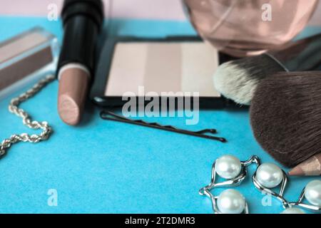 Ensemble de cosmétiques pour femmes en rouge à lèvres, surligneur, doublure pour lèvres, brosses, brosses, parfum, poudre, bijoux sur fond bleu. Coffret beauté plat. T Banque D'Images