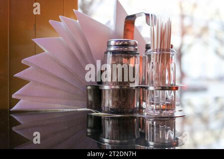 Verre poivre et sel shaker, cure-dents et serviettes sur la table dans le café en face de la fenêtre dans la soirée. Banque D'Images