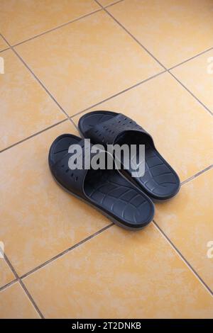 Une paire de pantoufles en caoutchouc ou en plastique pour hommes sur le sol carrelé d'une salle de bains d'appartement. Vue de dessus, gros plan, pas de gens. Banque D'Images