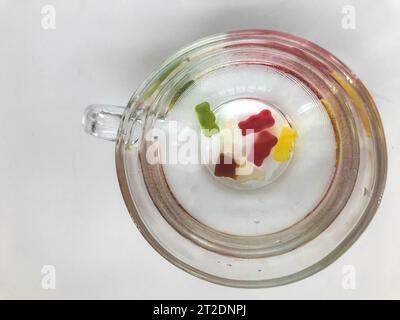 mug transparent, rond et grand, rempli d'eau. au fond de la tasse se trouvent des ours gommeux. les ours de couleurs jaune, rouge, vert nagent dans l'eau. m Banque D'Images