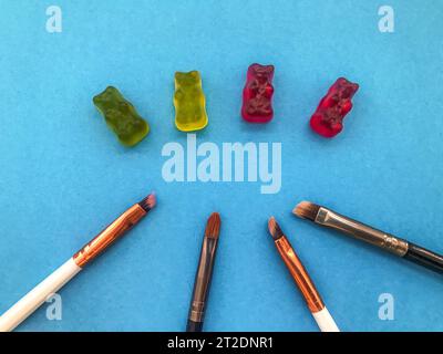 les pinceaux de maquillage reposent sur un fond bleu mat à côté des ours gommeux. travail manuel. chefs-d'œuvre culinaires. livre de coloriage d'ours dans des couleurs vives. gummy Banque D'Images