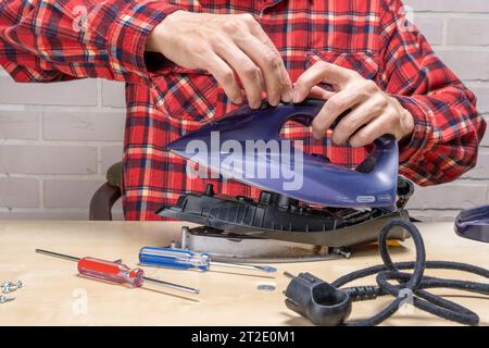 le fer à repasser est cassé. le maître répare le fer dans l'atelier sur la table à l'aide d'outils. Fer électrique démonté. Banque D'Images