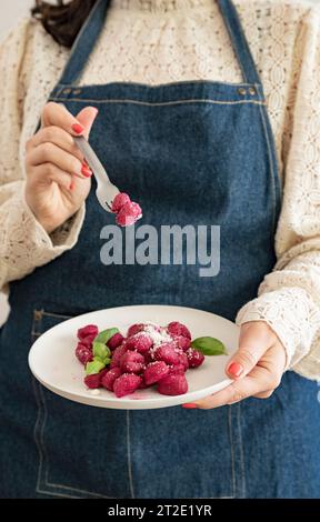 Betterave gnocchi italienne. La nourriture traditionnelle italienne dans un bol est tenue par une femme dans un tablier. Boulettes de pommes de terre faites à la main avec parmesan et betteraves. Nourriture pour les végétariens et les amateurs de cuisine italienne typique Banque D'Images