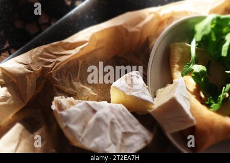 Camembert et crêpe sur papier parchemin et planche de bois Banque D'Images