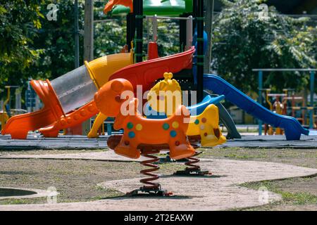 Chevaux à bascule colorés et toboggans dans l'aire de jeux. Aire de jeux extérieure pour enfants dans la cour. Banque D'Images
