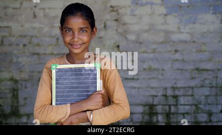 Portrait de la petite fille indienne mignonne heureuse en uniforme scolaire tenant l'ardoise vierge, adorable enfant élémentaire montrant le tableau noir. concept d'éducation de l'enfant. Banque D'Images