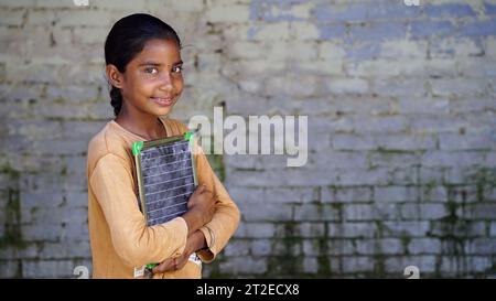 Portrait de la petite fille indienne mignonne heureuse en uniforme scolaire tenant l'ardoise vierge, adorable enfant élémentaire montrant le tableau noir. concept d'éducation de l'enfant. Banque D'Images