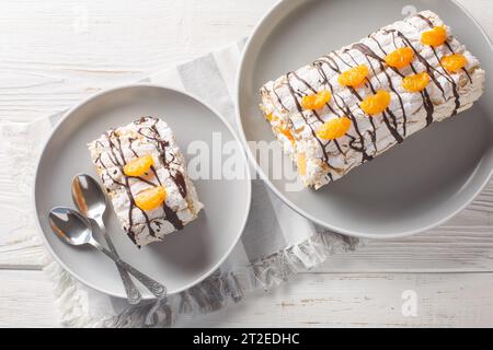 Délicieux dessert suédois maison gâteau roulé Budapest rempli de crème fouettée et mandarines en gros plan dans une assiette sur la table. Vue de dessus horizontale fr Banque D'Images