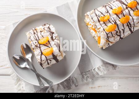 Dessert suédois traditionnel sans gluten rouleau Budapest rempli de crème fouettée et de mandarines en gros plan dans une assiette sur la table. Vue de dessus horizontale f Banque D'Images