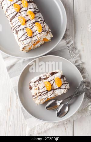 Gâteau roulé Budapest classique sans gluten avec mandarines closeup sur l'assiette sur la table. Vue verticale de dessus Banque D'Images