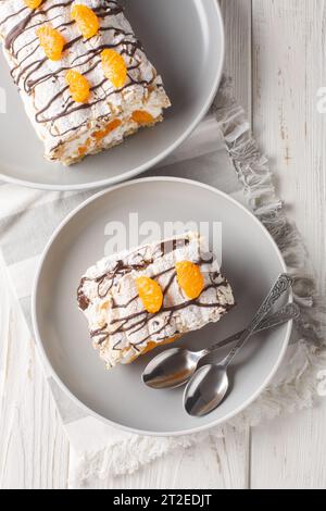Dessert suédois rouleau Budapest rempli de crème fouettée et mandarines en gros plan dans une assiette sur la table. Vue verticale de dessus Banque D'Images