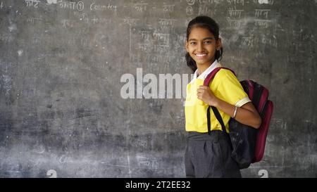 Fille d'école rurale indienne souriante avec sac à dos regardant la caméra. Enfant joyeux portant l'uniforme scolaire avec un grand sourire. École primaire et primaire Banque D'Images