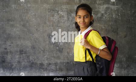 Fille d'école rurale indienne souriante avec sac à dos regardant la caméra. Enfant joyeux portant l'uniforme scolaire avec un grand sourire. École primaire et primaire Banque D'Images