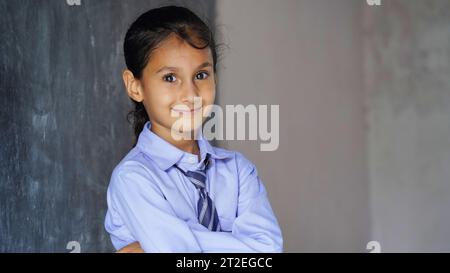 Portrait de joyeux enfant d'école indienne ou des enfants en uniforme levant la main dans la salle de classe tout en étudiant avec des livres et un ordinateur portable. Apprentissage en ligne Banque D'Images