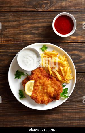 Schnitzel weiner pané avec frites de pommes de terre et sauce sur fond de bois. Vue de dessus, pose à plat Banque D'Images