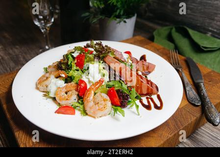 Une salade de crevettes frites, une vinaigrette au vinaigre balsamique, des poires trempées dans du vin rouge servies sur une assiette blanche dans un restaurant. Banque D'Images