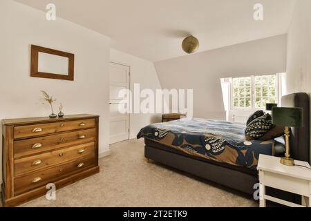 une chambre avec un lit, une commode et un miroir sur le mur en face de la chambre est de couleur très blanche Banque D'Images