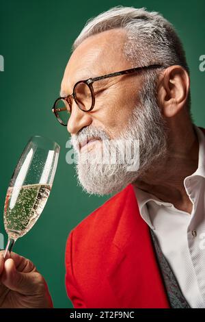 Portrait du Père Noël avec barbe blanche et verres profitant du champagne sur fond vert, concept d'hiver Banque D'Images