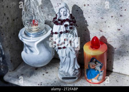 Bougies électriques kitschy alimentées par piles à côté d'une petite figure enveloppée de chapelet de Marie sur une tombe d'urne dans un cimetière, Bari Sardo, Ogliastra Banque D'Images