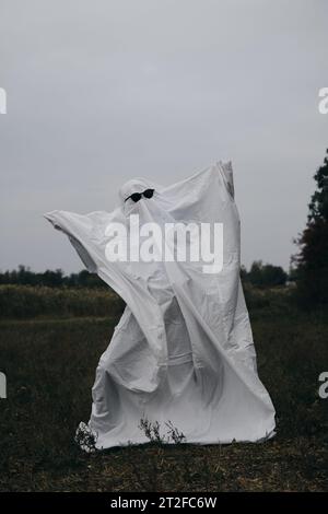 Costume créatif Halloween pour un adulte. Un fantôme d'un drap blanc avec des lunettes de soleil noires dansant dans un champ d'automne. Concept Trick or Treat. Banque D'Images