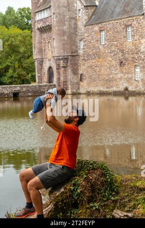 Un jeune père avec son bébé visitant le château médiéval au bord du lac Trecesson, commune de Campeneac dans le département du Morbihan, près de la Brocéliande Banque D'Images