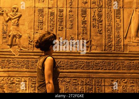 Une jeune femme regardant des dessins égyptiens et des hiéroglyphes au temple de Kom Ombo, le temple dédié aux dieux Sobek et Horus. En ville Banque D'Images