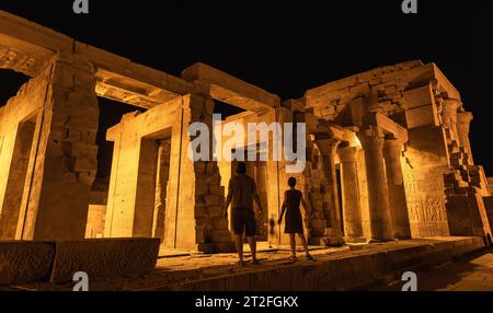 Un couple de touristes entre les colonnes de nuit du temple de Kom Ombo en robe traditionnelle, le temple dédié aux dieux Sobek et Horus. Banque D'Images