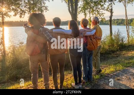 Cinq jeunes amis millénaires multiraciaux sur une randonnée célèbrent atteindre un sommet près de la côte, en regardant la beauté de la nature et le soleil longueur, vue de côté. Photo de haute qualité Banque D'Images