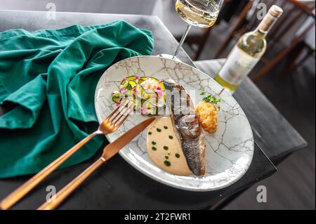 Bar ou filet de dorado avec courgettes cuites au four et sauce sur une assiette grise dans un restaurant Banque D'Images