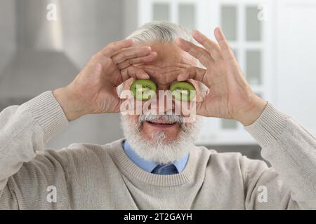 Homme âgé couvrant les yeux avec des moitiés de kiwi à l'intérieur Banque D'Images