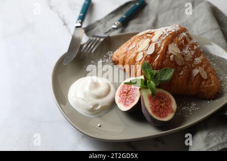 Délicieux croissant avec figue, flocons d'amande et crème sur table blanche, gros plan Banque D'Images