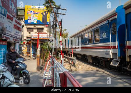 Un train des chemins de fer du Vietnam passe des gens à moto et à vélo à un passage à niveau (passage à niveau) à Hanoi, Vietnam. Banque D'Images