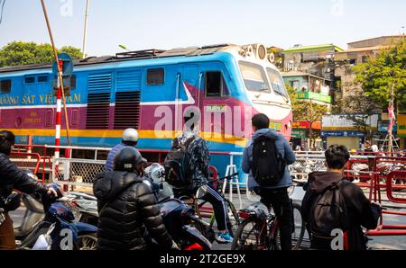 Un train des chemins de fer du Vietnam passe des gens à moto et à vélo à un passage à niveau (passage à niveau) à Hanoi, Vietnam. Banque D'Images