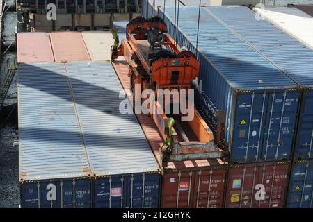 Des conteneurs fixés à l'épandeur de grues portiques actionnées par des débardeurs sont chargés sur le navire. Banque D'Images