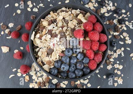 Muesly avec des framboises et des myrtilles dans un bol noir sur fond sombre. Banque D'Images