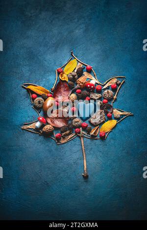 Les feuilles d'automne, les baies de rowan, les cônes sont disposés en forme de feuille d'érable sur fond bleu. Créatif, concept d'automne Banque D'Images