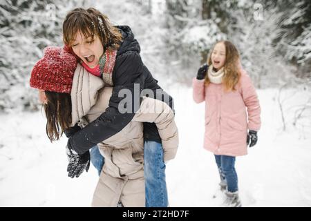 Sœurs adolescentes drôles et leur mère s'amusant sur une promenade dans la forêt de pins couverte de neige sur la journée froide d'hiver. Adolescentes explorant la nature. Actus hivernaux Banque D'Images