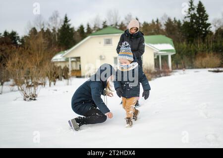 Adorable garçon en bas âge et ses sœurs aînées s'amusant dans une cour arrière le jour d'hiver enneigé. Enfants mignons portant des vêtements chauds jouant dans une neige. Hiver Banque D'Images