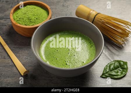 Tasse de thé matcha frais, poudre verte, cuillère et fouet en bambou sur table gris foncé, gros plan Banque D'Images