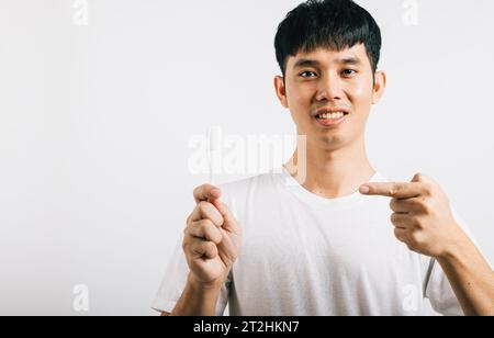 L'homme asiatique se brosse les dents le matin, tient une brosse à dents, sourit et pointe Banque D'Images