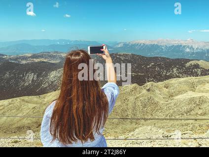 une fille dans une robe blanche avec de longs cheveux foncés sur la plate-forme d'observation fait un selfie. photo de vous avec en toile de fond une belle vie de grande hauteur Banque D'Images