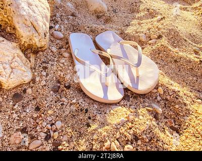 des pantoufles en caoutchouc blanc se tiennent sur le sable. chaussures de mer. ardoises pour marcher le long de la côte de la mer. pantoufles pour femmes qui se portent sur un doigt. Banque D'Images