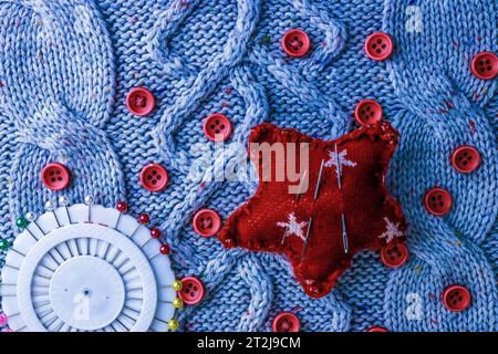 Belle texture d'un pull naturel doux et chaud, tissus tricotés et petits boutons ronds rouges pour la couture et un tapis d'aiguilles. Pose à plat. L'arrière-plan. Banque D'Images